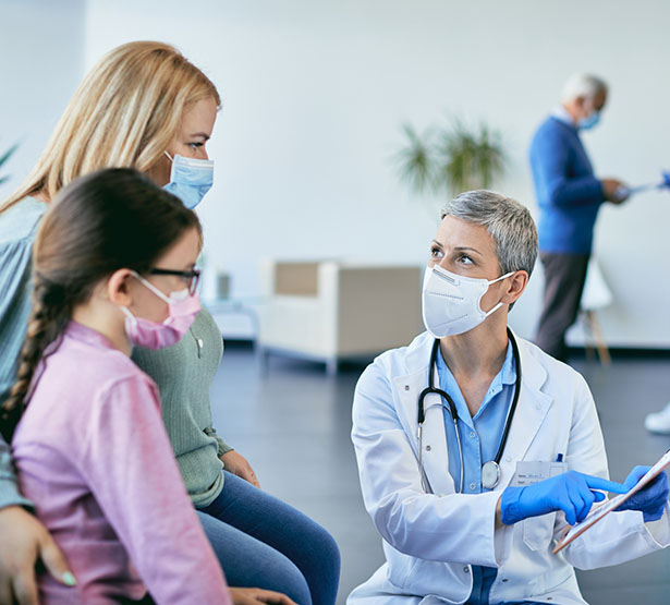 Une femme médecin montre un document à une mère et son enfant dans un couloir - MACSF