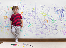 Un enfant, adossé au mur sur lequel il vient de dessiner, regarde son parent d'un air désolé - MACSF