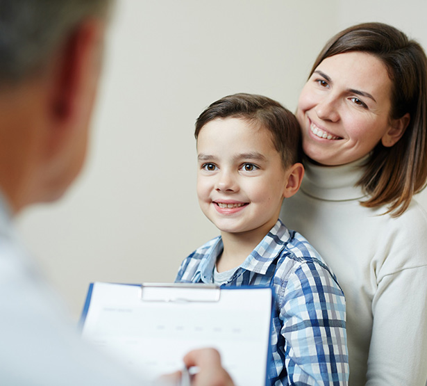 Un jeune garçon assis sur les genoux de sa mère regarde le médecin - MACSF