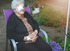 Une dame âgée portant un cache oeil est assise dans le jardin - MACSF