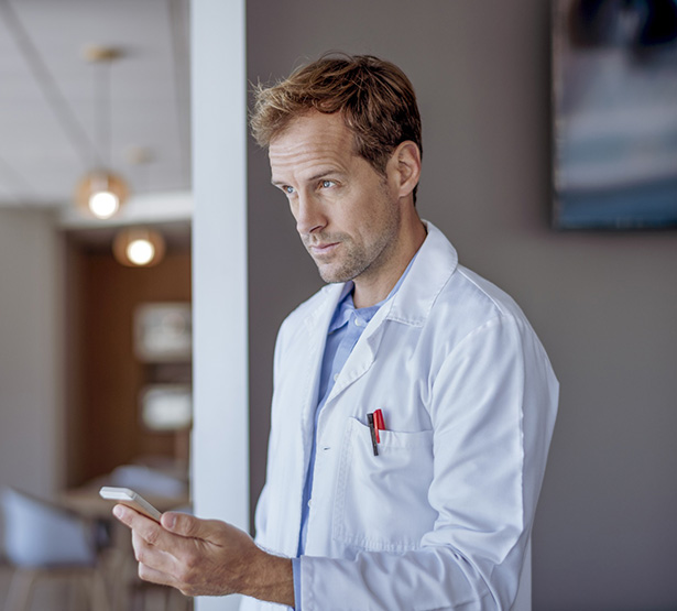 Un homme médecin tient un téléphone à son domicile - MACSF