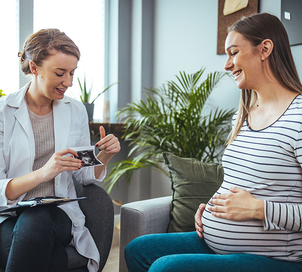 Une jeune femme sourit en regardant l'échographie que lui montre la sage-femme - MACSF