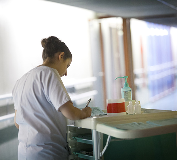 Une infirmière dans un couloir note les soins effectués - MACSF