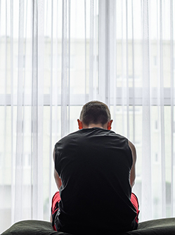 Un homme déprimé assis sur le bord de son lit devant la fenêtre - MACSF