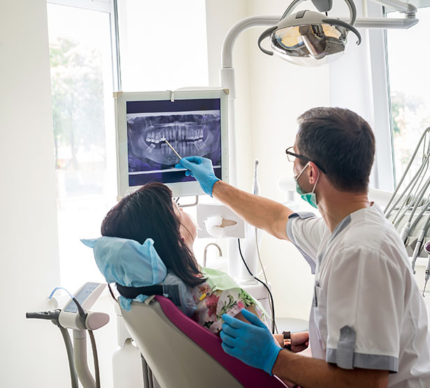 Un chirurgien-dentiste montre une dent sur l'écran à une patiente - MACSF