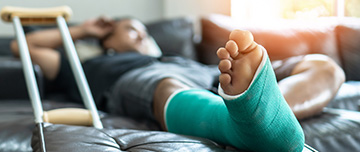 Un homme avec un plâtre à la jambe installé sur son canapé - MACSF