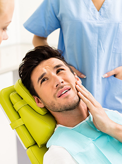 Un jeune homme installé sur le fauteuil du dentiste se tient la joue - MACSF