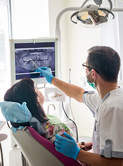 Un chirurgien-dentiste montre une dent sur l'écran à une patiente - MACSF