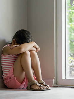 Une jeune fille maltraitée assise près d'une fenêtre | MACSF