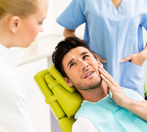 Un jeune homme installé sur le fauteuil du dentiste se tient la joue - MACSF