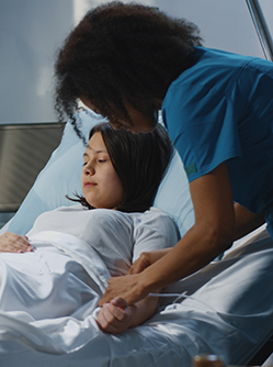 Jeune femme alitée à l'hôpital, entourée de deux soignants - MACSF